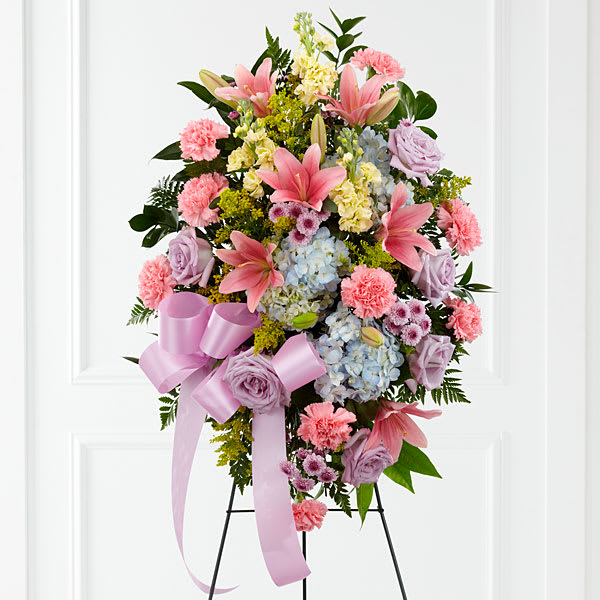 The FTD Blessings of the Earth Easel - The FTD&reg; Blessings of the Earth&trade; Easel is a soft and serene arrangement that elegantly honors the life of the deceased. Lavender roses pink carnations pink Asiatic lilies blue hydrangea yellow stock lavender button poms solidago and lush greens are beautifully accented with a lavender satin ribbon and displayed on a wire easel to create a gorgeous display for their memorial service.