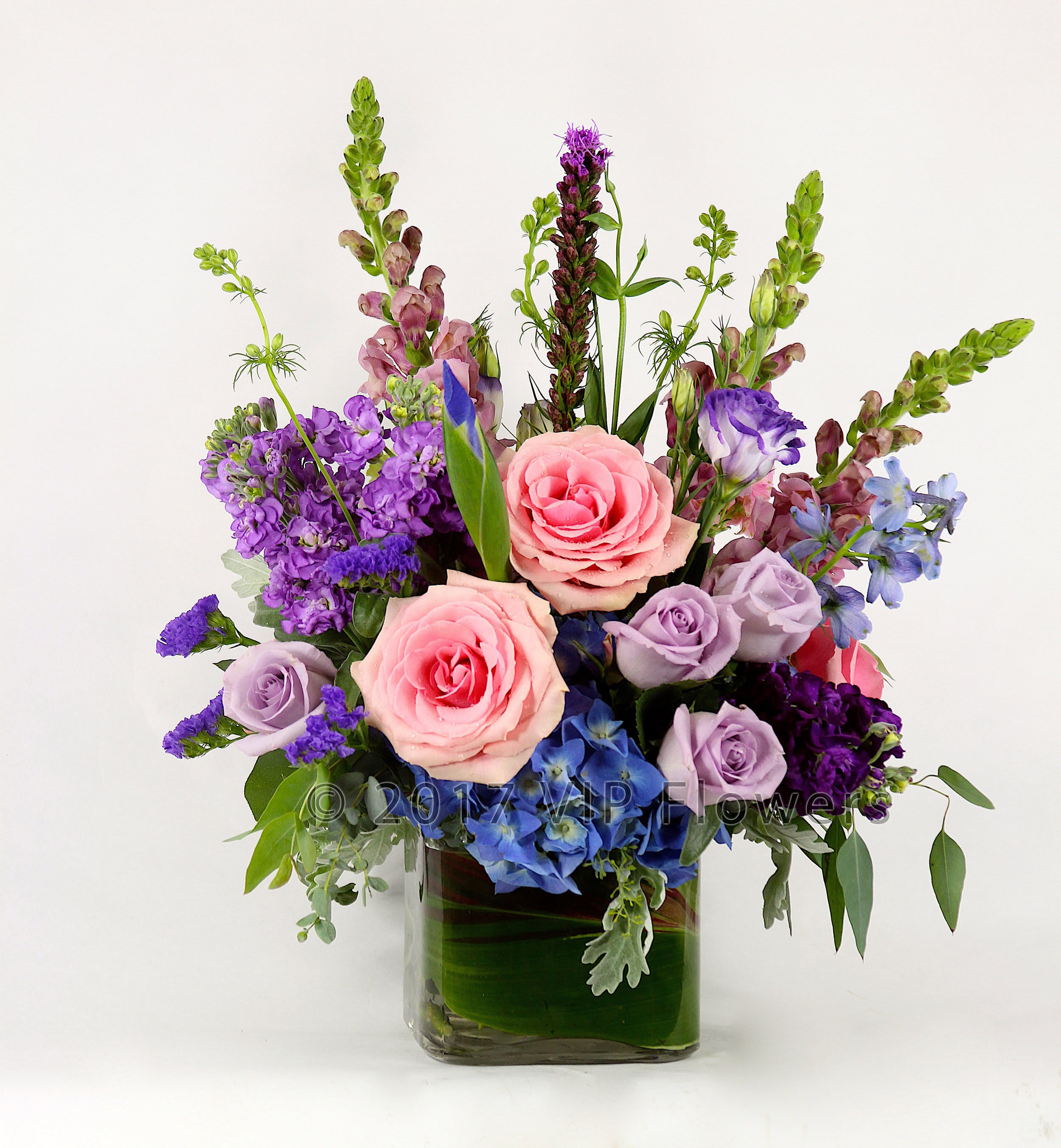 A Flower Cluster - Flowers Included:  Pink Roses Purple Roses Blue Hydrangea Purple Stock Pink Snapdragons Liatris  Seasonal Greens Iris       Substitutions may be necessary to ensure your arrangement or specialty gift is delivered in a timely manner. The utmost care and attention is given to your order to ensure that it is as similar as possible to the requested item (Please note that some flowers and colors may vary due to seasonality.)