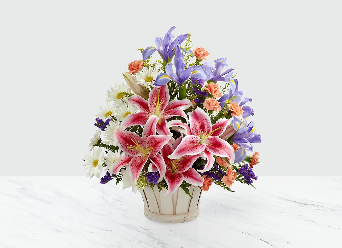 The Wondrous Nature™ Bouquet The Wondrous Nature™ Bouquet - The Wondrous Nature™ Bouquet is bountifully bedecked with a dazzling display of color and beauty. Stargazer lilies stretch their fuchsia petals out amongst an arrangement of blue iris, white traditional daisies, orange mini carnations, purple statice and yellow solidago in a round whitewash handled basket, creating a delightful bouquet your special recipient will adore BEST bouquet approximately 17"W x 14"W. Lilies may arrive in various stages of development. The lily blooms will continue to open, extending arrangement life - and your recipient's enjoyment..