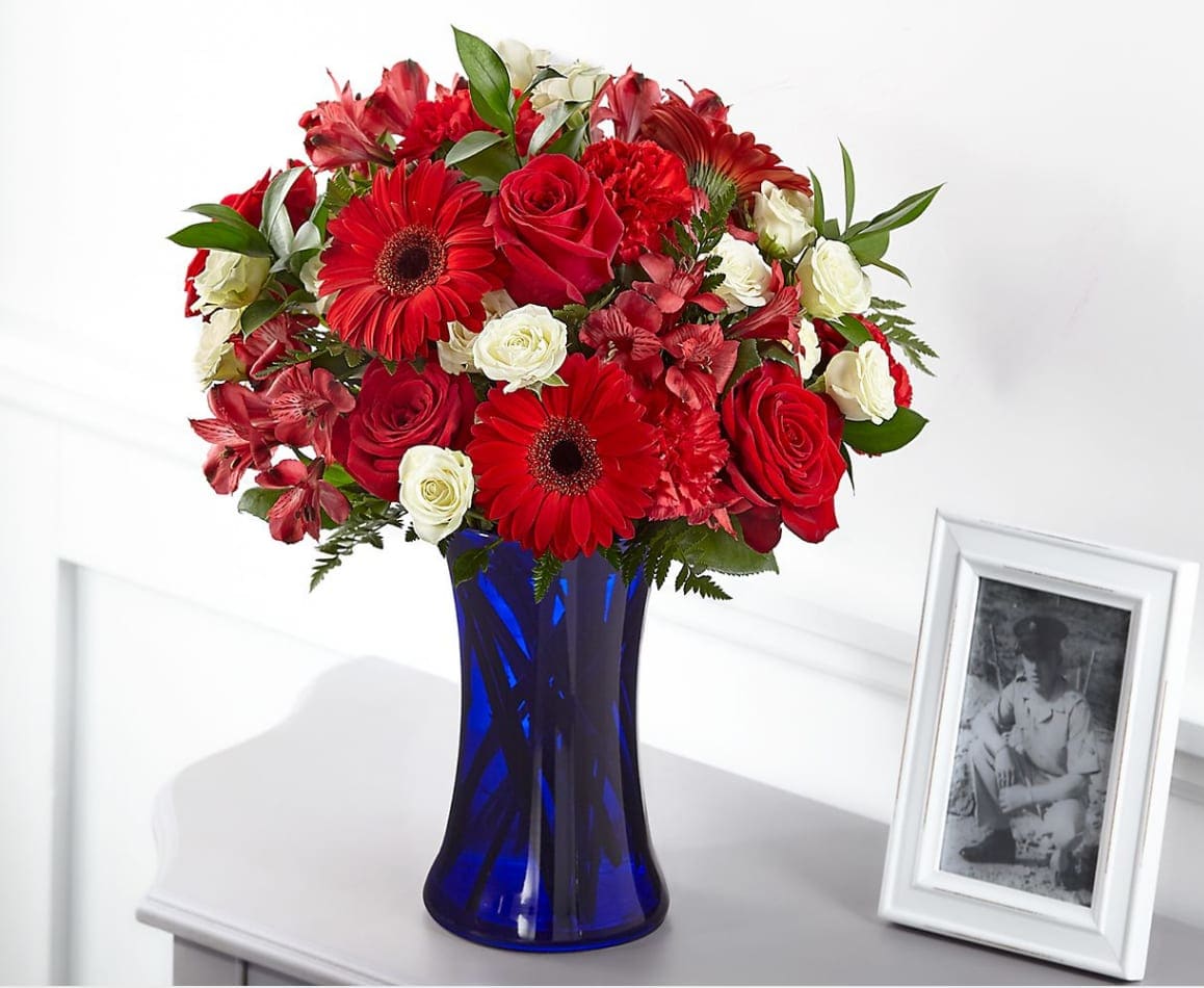 Hearts Embrace Bouquet Hearts Embrace Bouquet - The combination of red, white and blue pays patriotic tribute to the heroes in our lives who have passed. Our Hearts Embrace Bouquet is designed with roses, gerbera daisies, alstroemeria and carnations in a bold blue vase to share a gesture of healing respect.