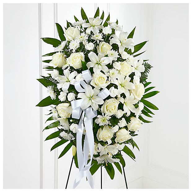 Exquisite Tribute™ Standing Spray - The Exquisite Tribute™ Standing Spray is an elegant display of sweet serenity. White roses, Asiatic lilies, chrysanthemums and mini carnations are artfully arranged amongst emerald palm fronds and lush greens. Accented by white satin ribbon and standing on a wire easel, this standing spray is an outstanding way to honor the life of your loved one.
