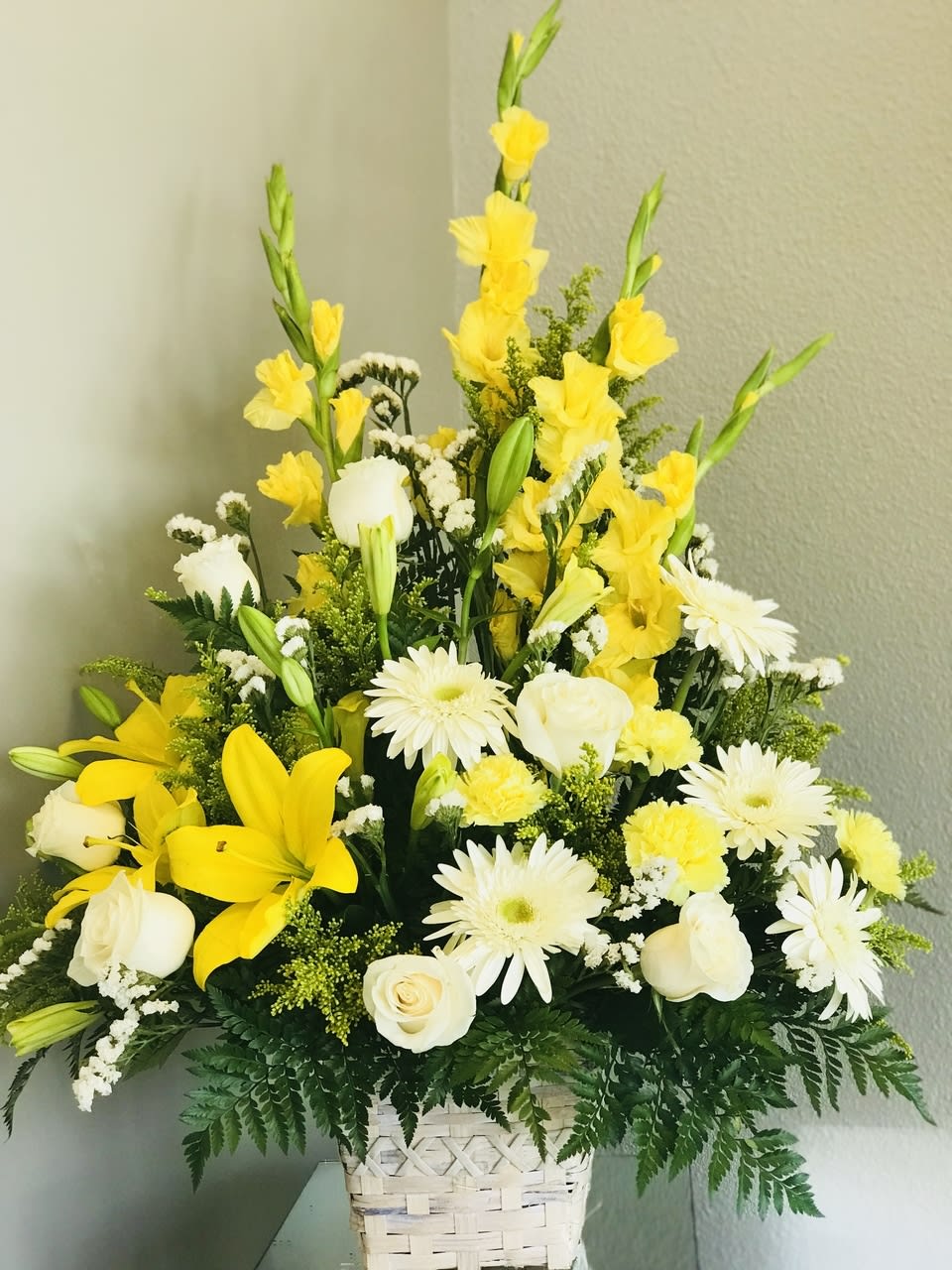 SAFF Sunshine Remembrance - A colorful assortment of our finest blooms. Crème de la Crème roses, yellow Asiatic lilies,white gerbera daisies, yellow gladiolus, yellow carnations, and white statice are accented with lush greenery. Gorgeously displayed in a basket, this arrangement will add to the natural beauty and serenity of their final tribute.