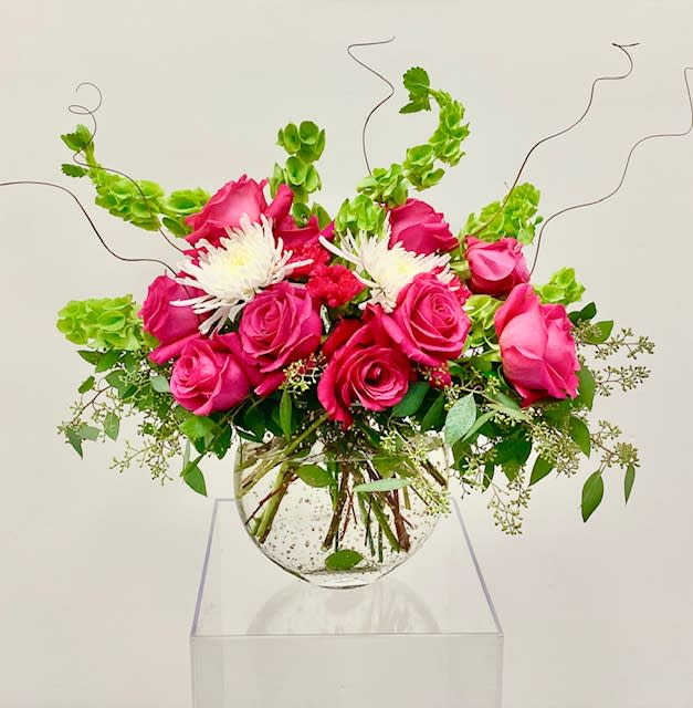 Pretty In Pink - Modern display of hot pink roses accented with Bells of Ireland, seeded eucalyptus, and spider mums.  Flowers set in a moon shaped clear vase.