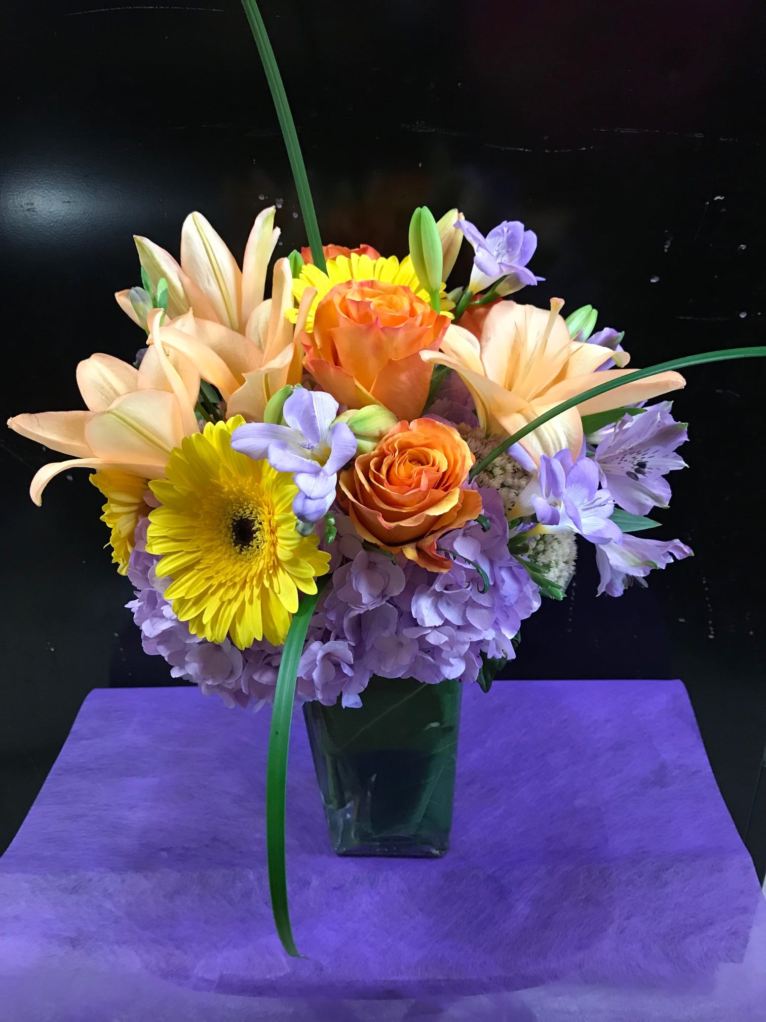 Brighter Days Ahead - Soft and cheerful arrangement sure to brighten anyone's day. Soft purple flowers accented with bright colored daisies, roses, and lilies. 