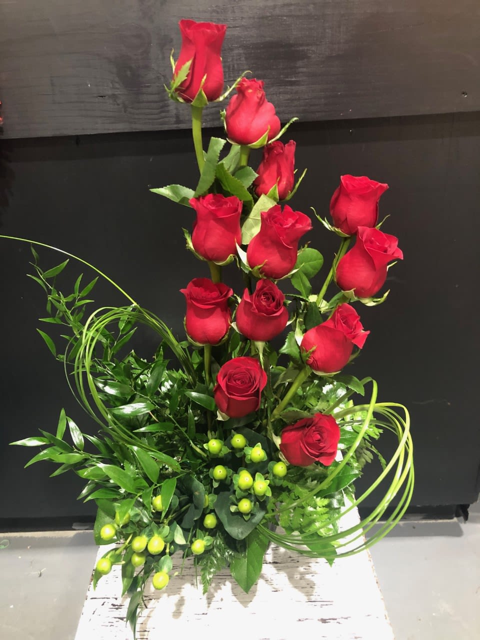 The Rose Swirl The Rose Swirl - Red Roses arranged in a sweeping swirl pattern adorned with mixed greens and coffee berries. A modern Twist!