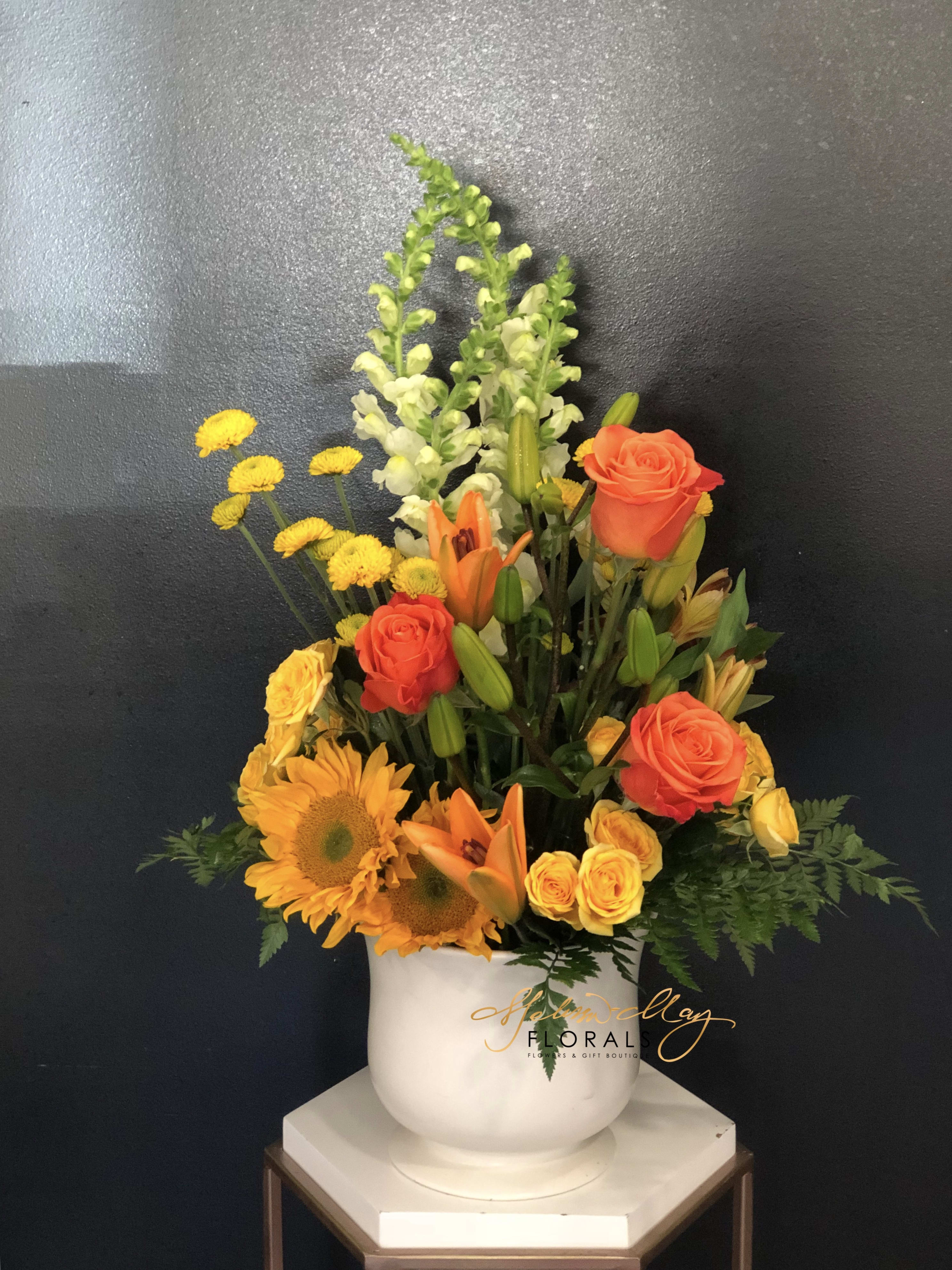 World of Treasures - We  all want to have all the treasures in the world, but that is not possible. We bring you a piece that will give you that feeling. Give someone this today, our fiery collection of snapdragons, Gerbera daisies, lilies and more rises gaily from an earthenware pot.  (Vase in image is no longer available. A substitute will be used.)