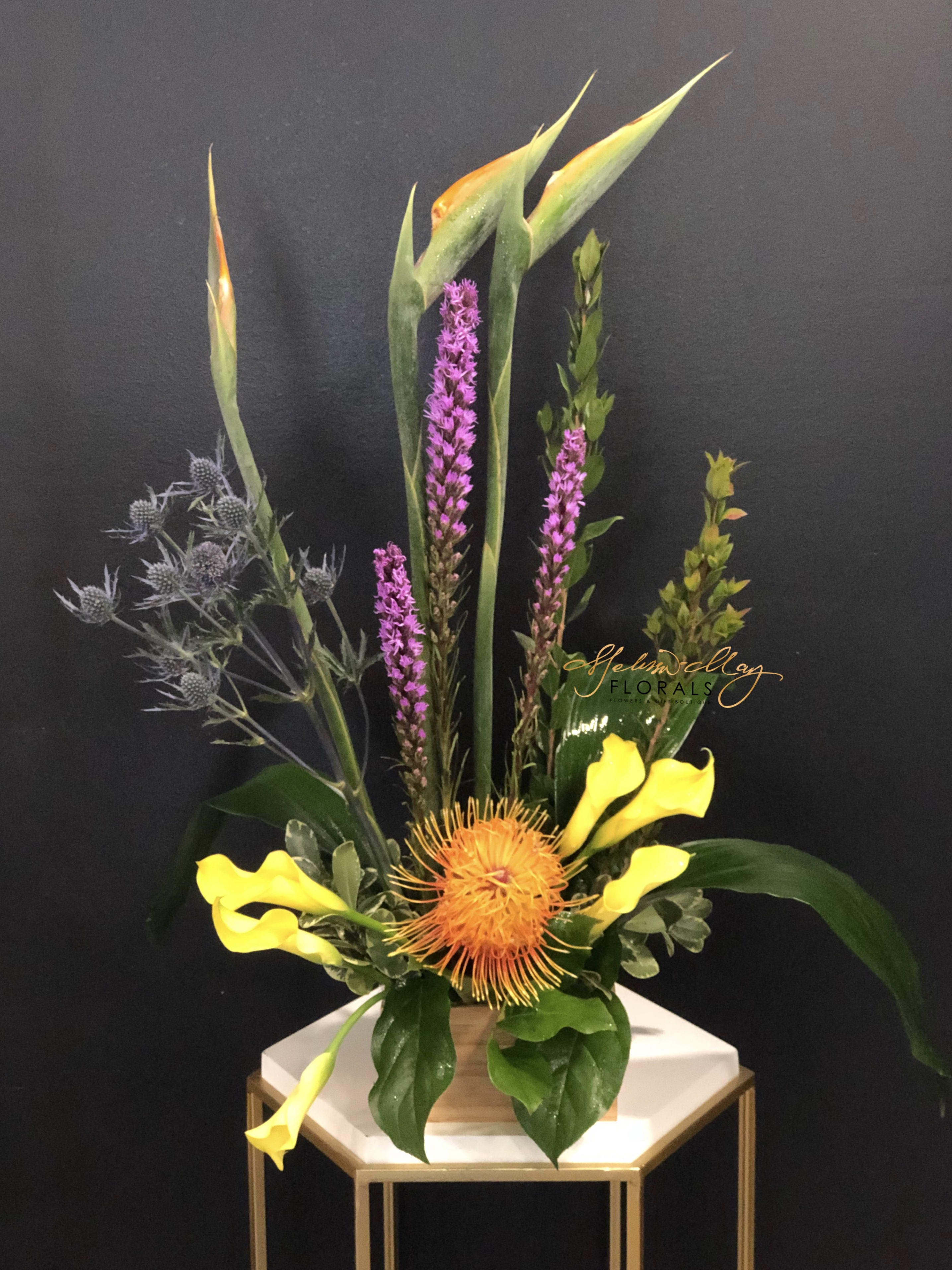 Blaze of Glory - This bold mix of exotic tropical elements, greenery and flowers soars upwards in a dramatic arrangement that will capture everyone’s attention! An interesting and long-lasting floral display that will brighten any room. Next day delivery is only allowed for this order.