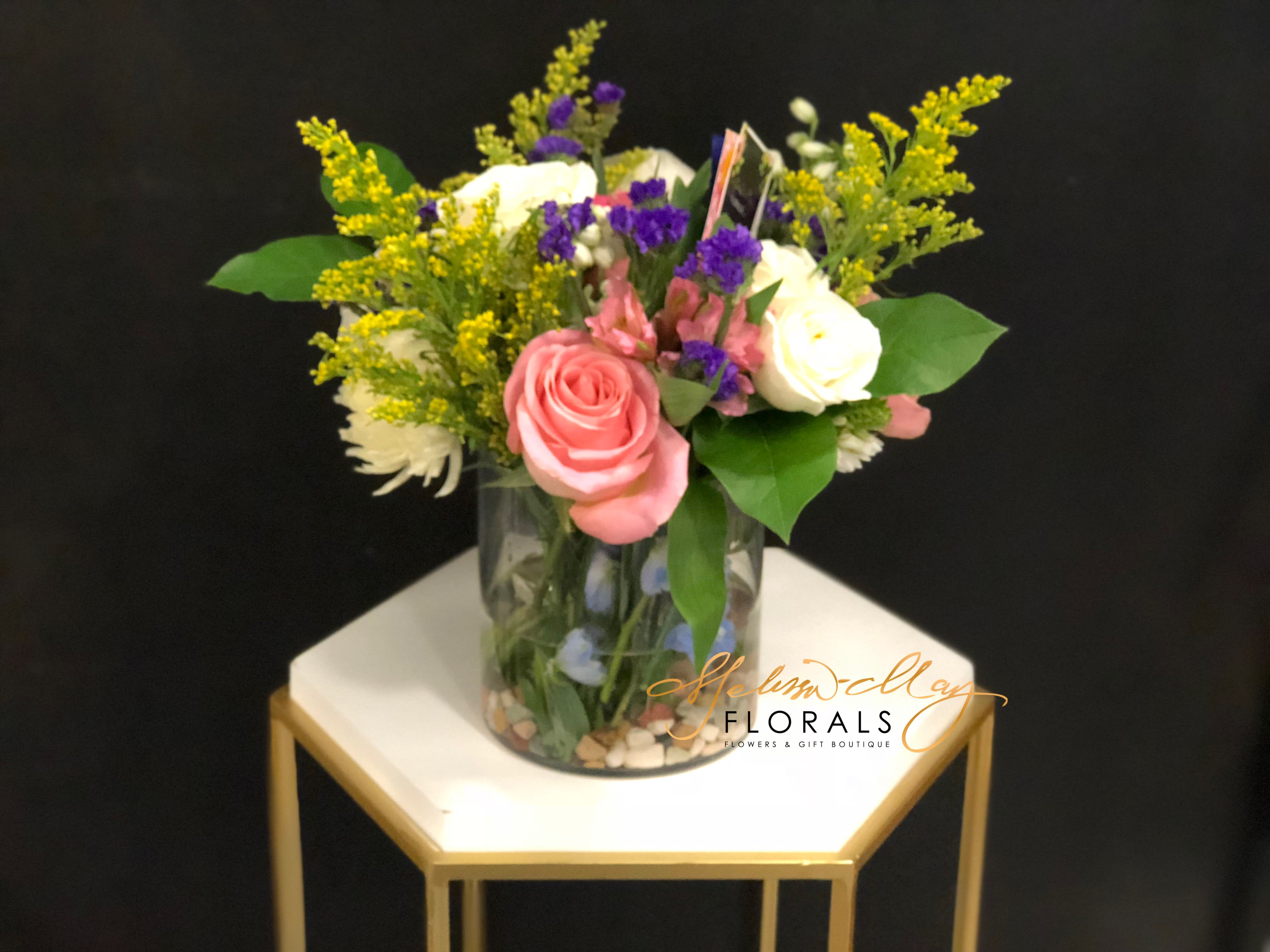 Sweet Memories - You’d like to surprise someone with gorgeous fresh flowers…a mix of blooms that looks as if the entire garden has been put into a vase! This splendid medley of blue, cream, white, pink and lavender flowers, presented on a bed of river rocks, is a beautiful choice.