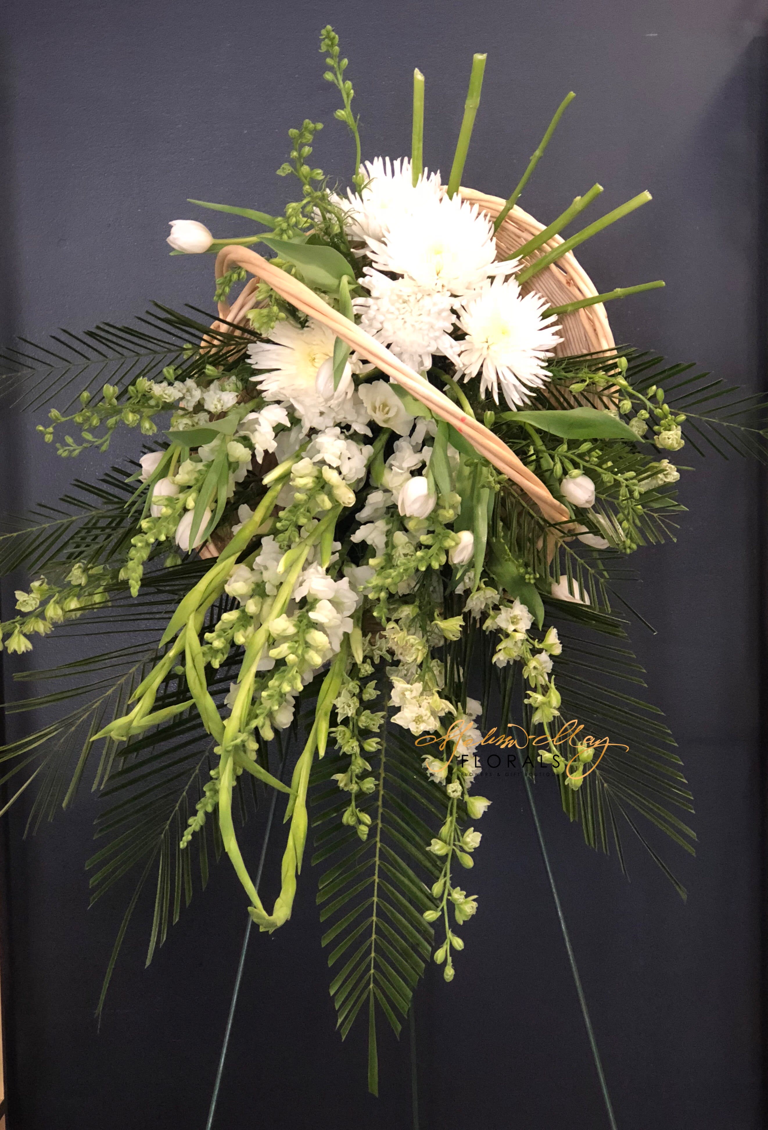All White Basket Standing Spray - A contemporary tribute, combining the warmth of a fireside basket with the drama of an easel display. Featuring gladiolus, larkspur, football mums, tulips and more. A basket filled with all the most beautifulest flowers from all over.