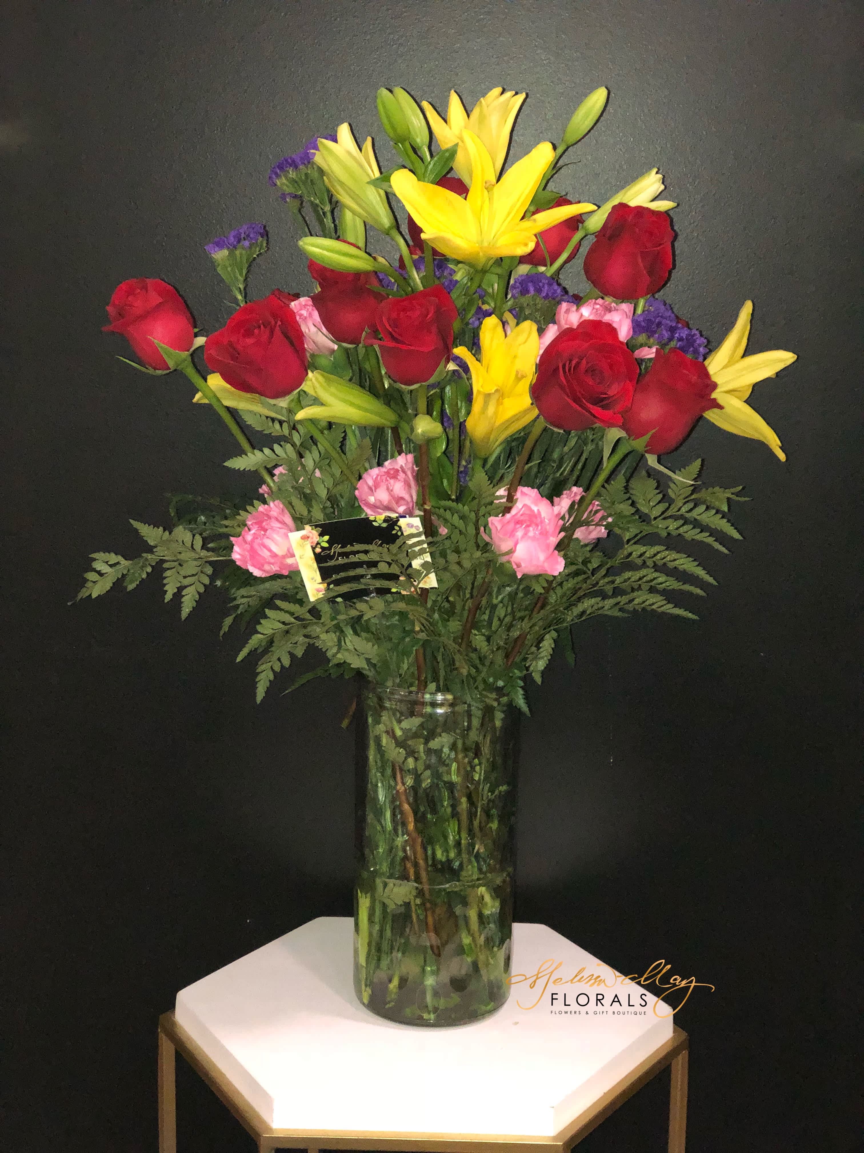 Dearly - Flowers speak to us in more ways you can ever imagine. They are the sweetest gift to give or have for yourself. An arrangement filled with red roses, pink carnations, and purple statices topping off with the yellow lilies. 