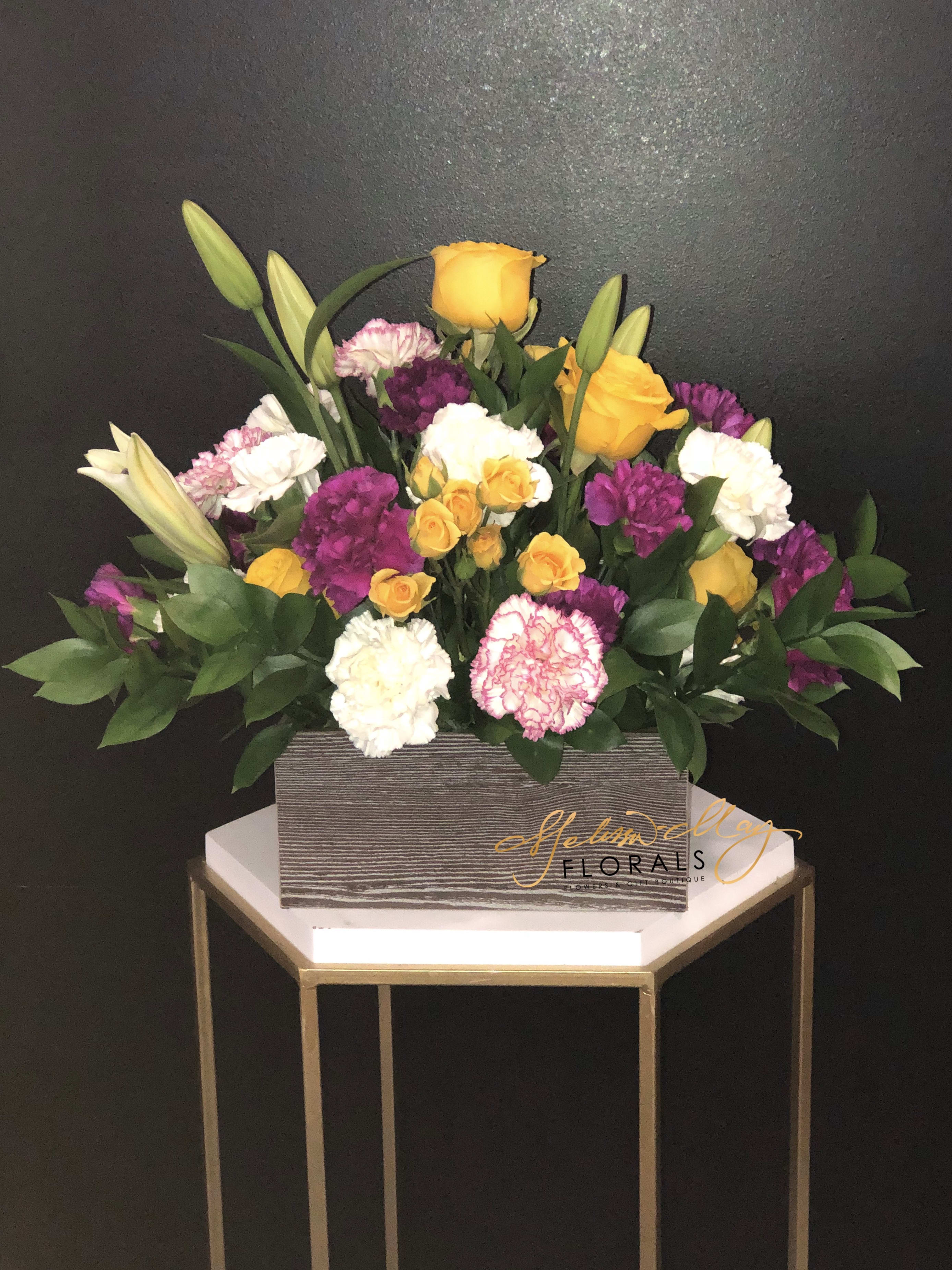 Garden of April - This beauty speaks to everyone. Your best friend would love to have this arrangement in their home. A perfect center piece to have at a brunch or even a dinner. Perfectly put together arrangement filled with carnations, soft spoken spray roses, and lovely lilies.   (Vase in image is no longer available. A substitute will be used.)