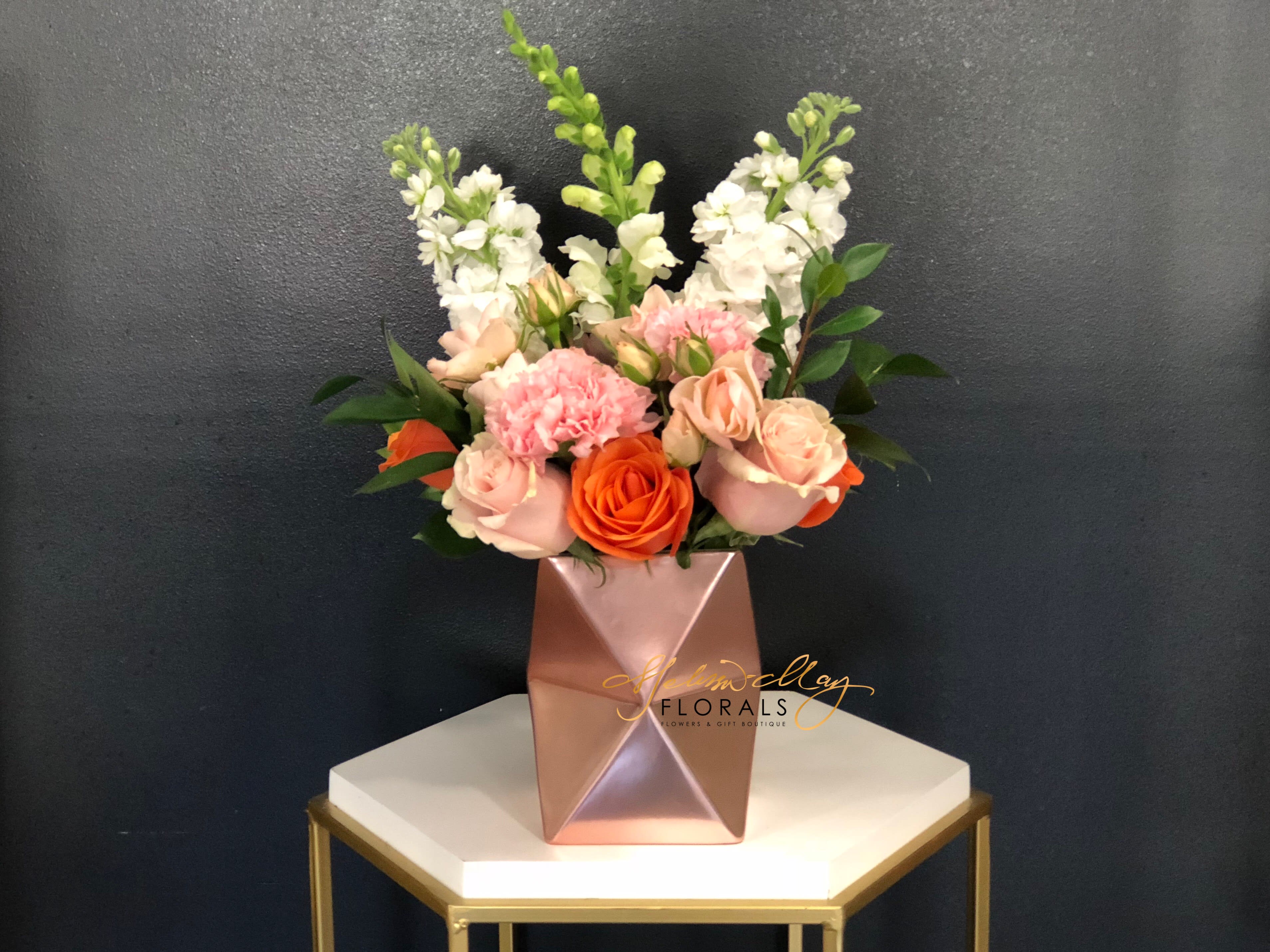 Blushing Beauty - There are so many pieces to show from but miss out on this one. An elegant piece that will have her blushing away. Its filled with pink and orange roses, pink carnations, and stock. Its filled with so much love and care. (Vase in image is no longer available. A substitute will be used.)  Disclaimer: (Candle in image is not included with order. Must be purchase separately.) 