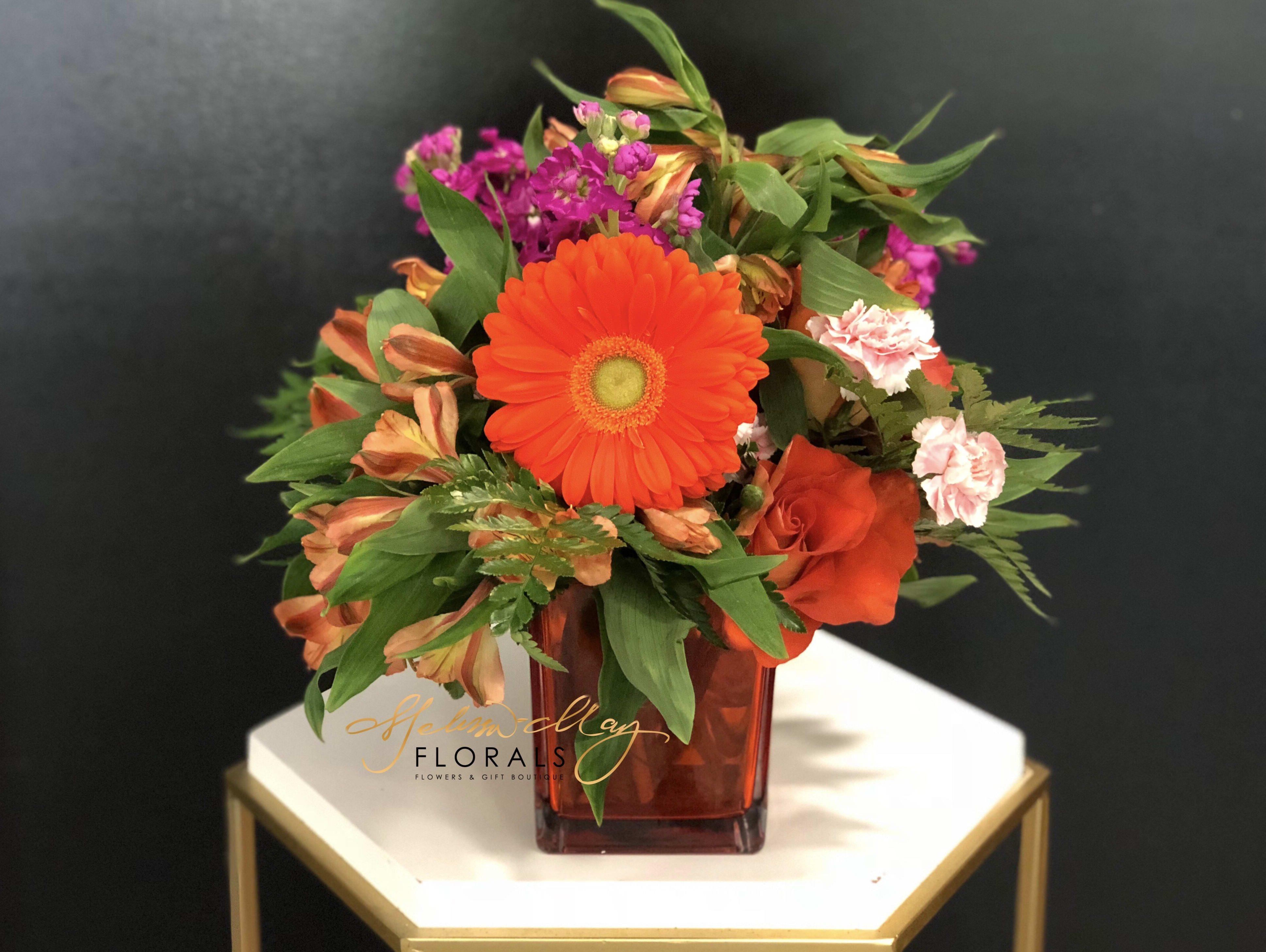 Orange Sprinkle - With a sprinkle of pink and purple assorted you will find a splash of orange throughout the arrangement. A little will have you fall in love with each other in this piece. We bring you orange Gerbera Daisies, purple stock, pink carnations, and so much more.  (Vase in image is no longer available. A substitute will be used.)