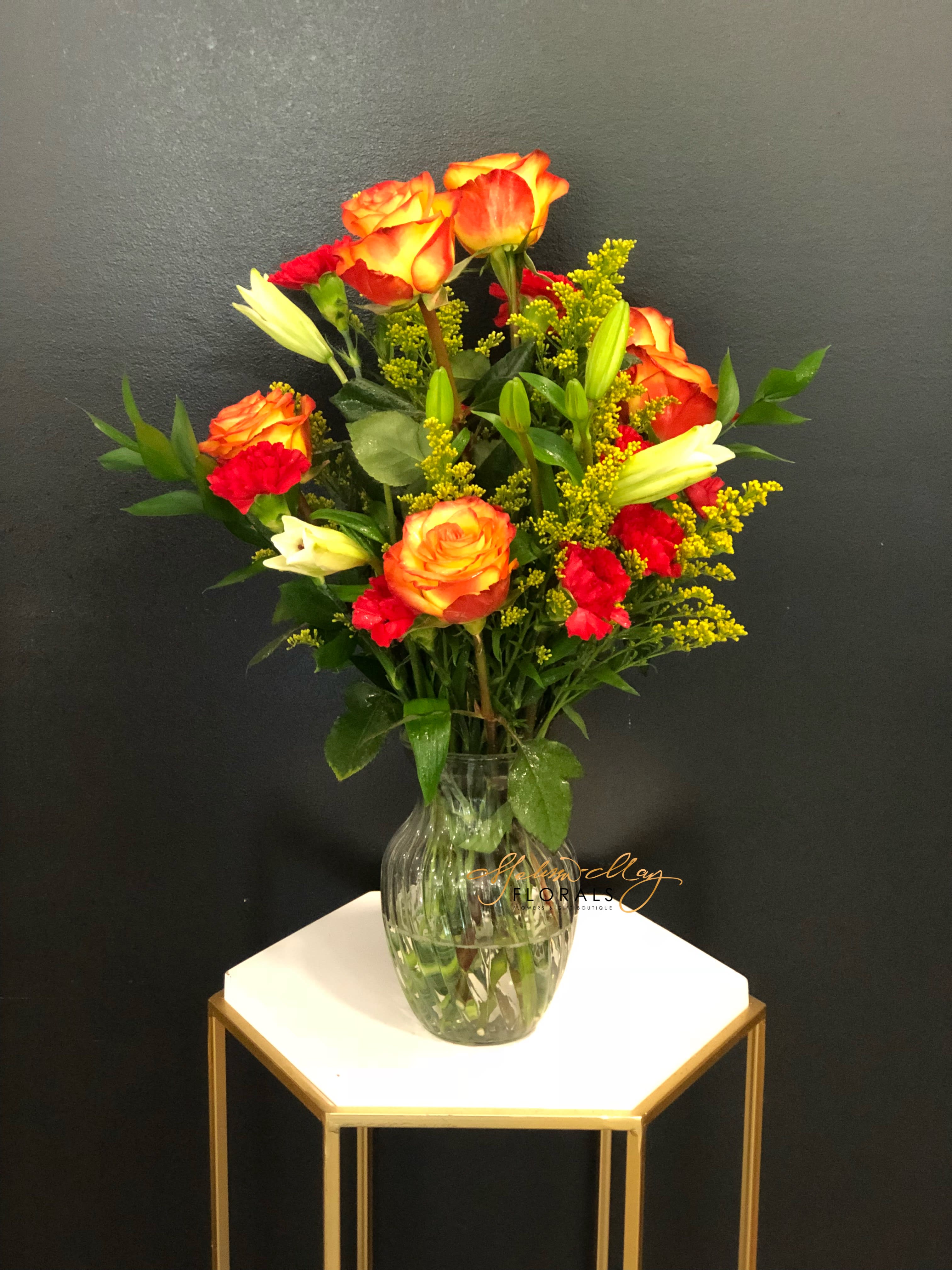 Fiery Bouquet - An bouquet that gives you fiery feelings of love all the way around. With orange roses and bright red carnations, lilies. All of which comes together in a clear vase. 