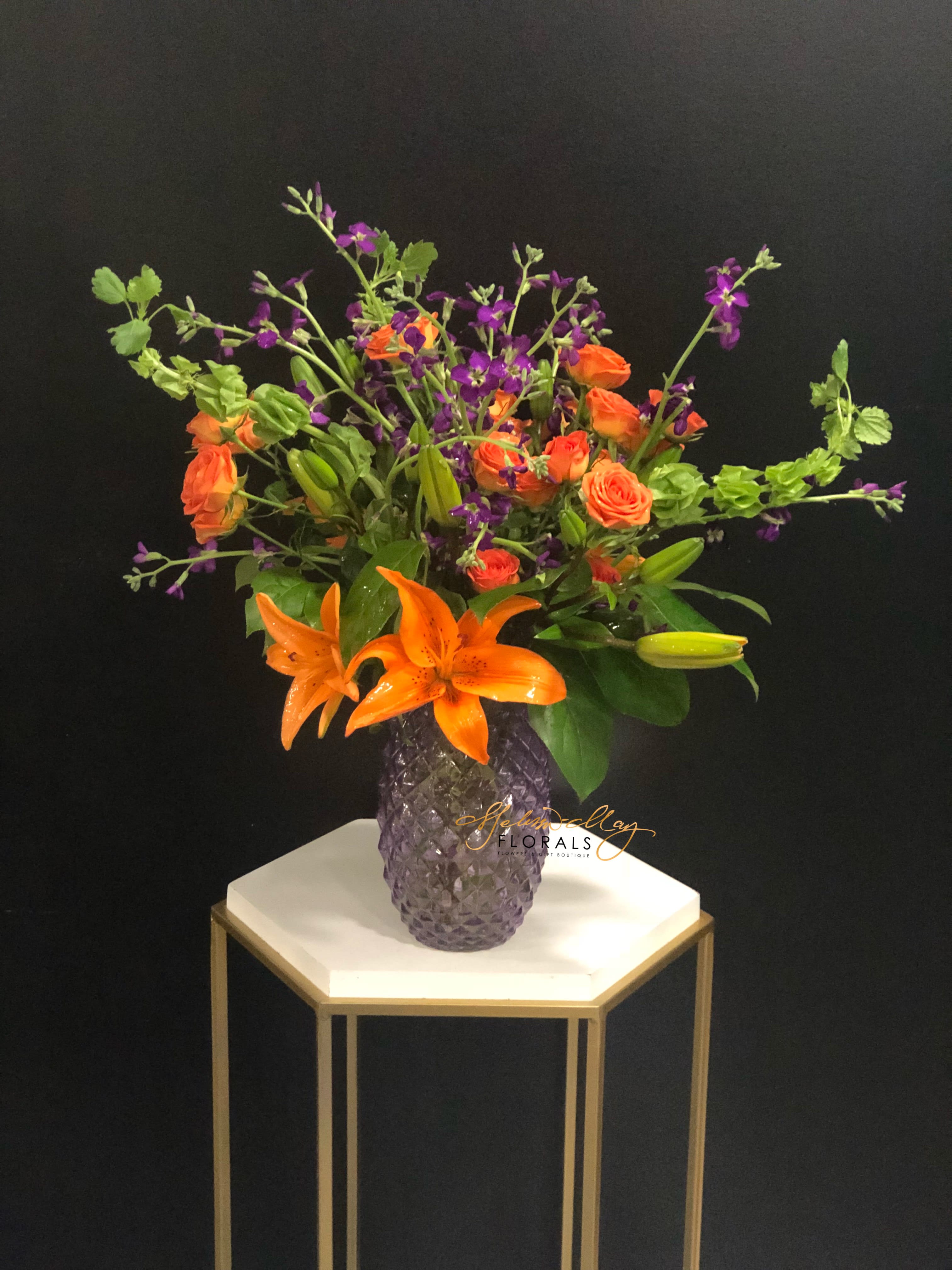 Forever Great - At time you want the world to know how great someone is. Why not show someone that you always see them to be the greatness individual in your life? She has bells of ireland, asiatic lilies, orange spray roses, and purple stock. 