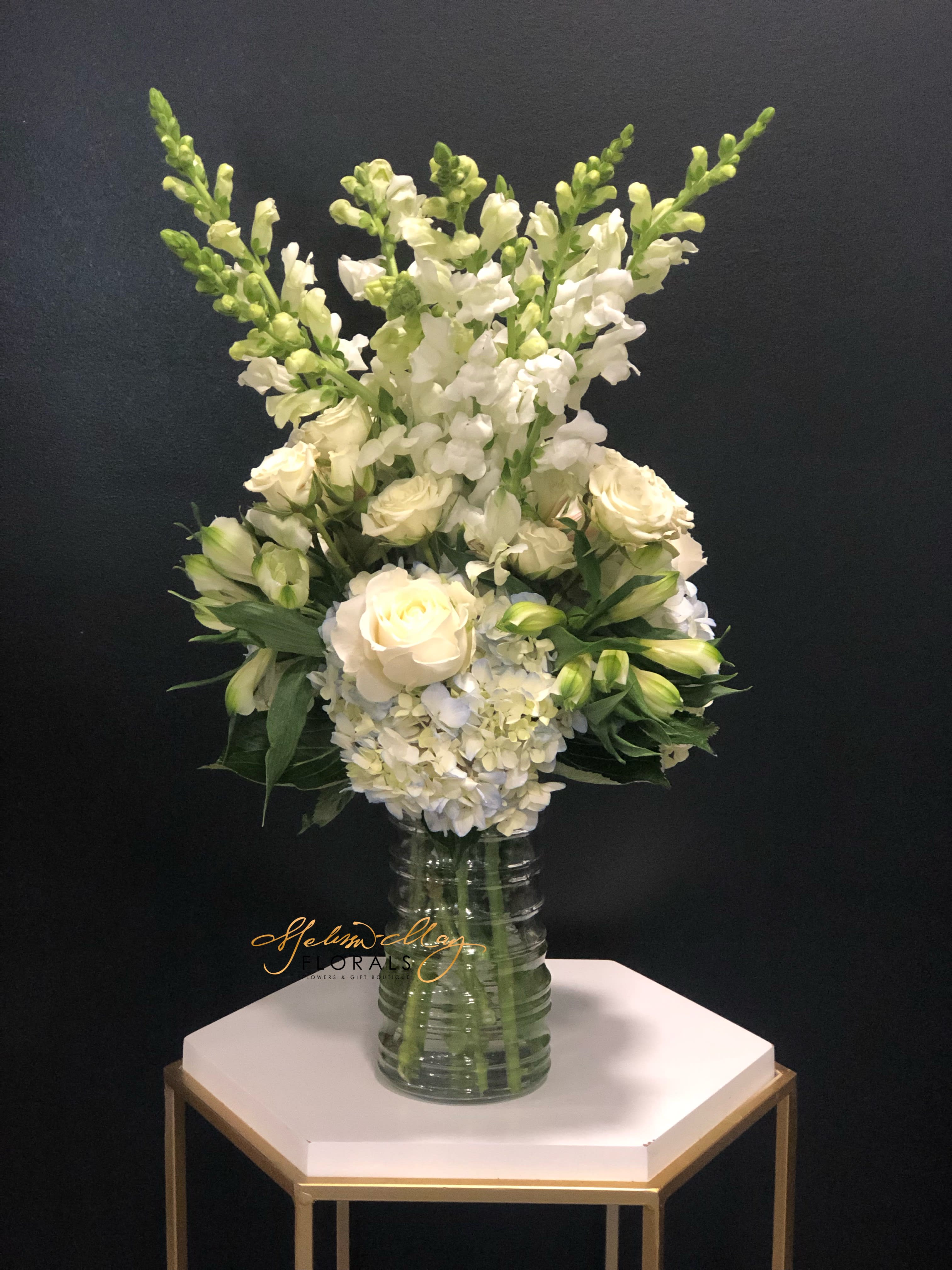 Wishful Yearning - This gorgeous soft-toned arrangement will bring back wishful feelings of magical days not forgotten. An elegant and aromatic white floral display of Spray Roses, Roses, Snapdragons and Light Blue Hydrangeas. Recall those sweet memories with the ones you love and show them how much you care with this thoughtful array.