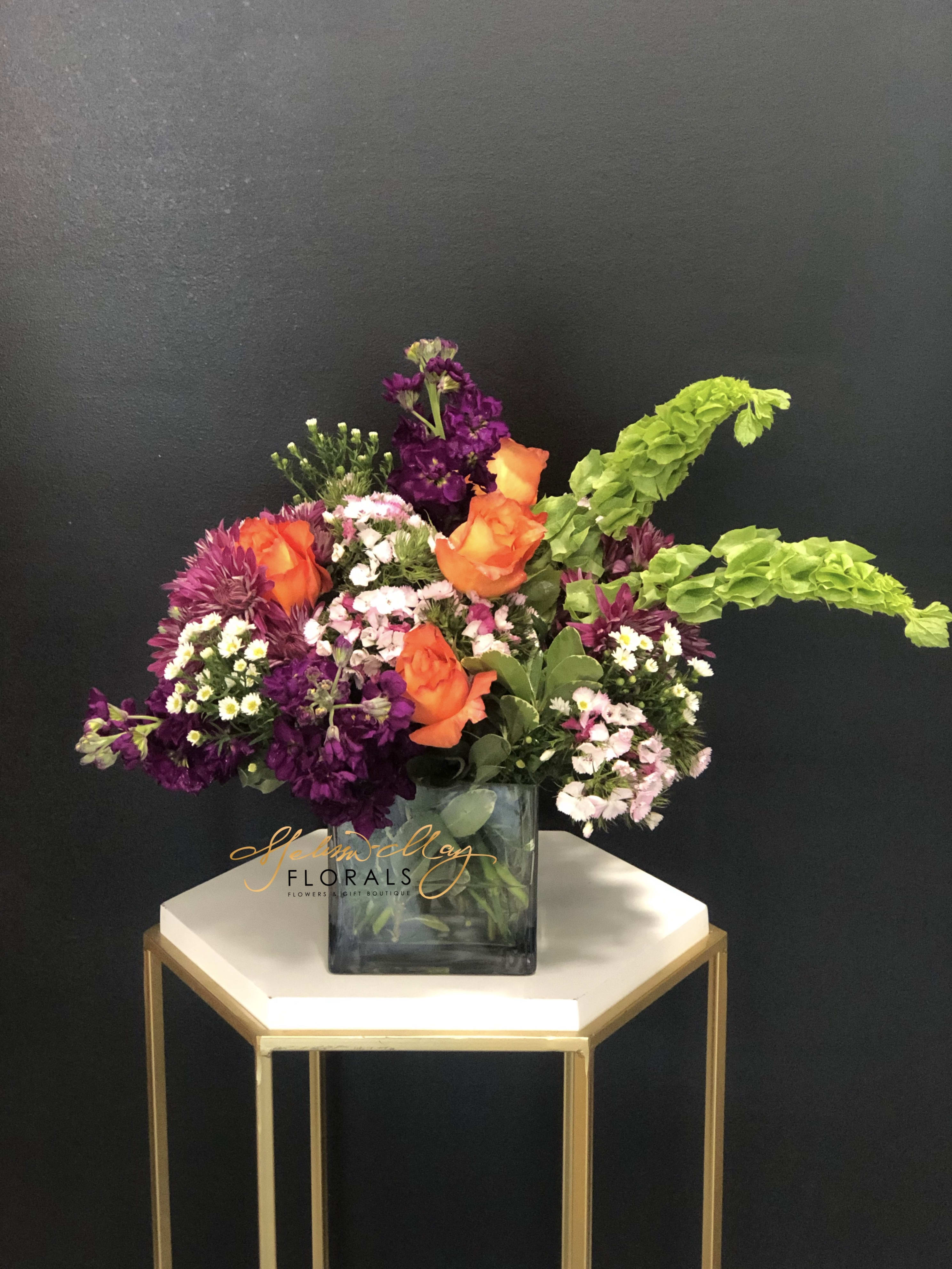 Forrest Flower  - This magnificent arrangement with deep purples and bright oranges will illuminate the smile on your loved ones face. Perfect for any fall occasion, anniversary, birthday or just because. This arrangement includes : Purple stock Bells of Ireland Orange Roses Mums And additional flowers with lush greenary