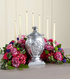 The FTD® Peaceful Thoughts™ Arrangement - Create a beautiful and reverential setting for an urn containing your loved one's cremated remains with an arc of lovely spring-hued blossoms that doubles as a candleholder. This respectful display gently draws the focus on a tabletop or altar for a memorial service, funeral or wake. The arrangement is hand-fashioned by a local FTD artisan florist of pink and lavender roses, hot pink carnations and purple statice and holds white taper candles (included). It has a flat bottom for stability and can also be used to enhance a display of a personal memento, religious statue or photograph.  Your purchase includes a complimentary personalized gift message.