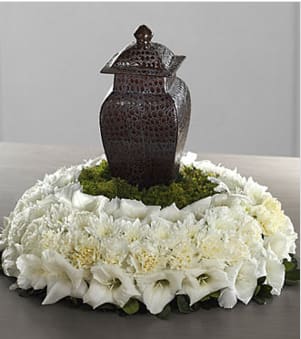 The FTD® Encircling Grace™ Arrangement The FTD® Encircling Grace™ Arrangement - A ring of heavenly white blossoms makes a beautiful, serene and dignified setting for an urn containing the cremated remains of a loved one. The tabletop wreath is constructed by a local FTD artisan florist of white cushion pompons atop a base of variegated greens with a flat bottom for stability when displayed. Its design allows for multiple options for display include enhancing a religious statue, personal memento, photograph or candleholder. Your purchase includes a complimentary personalized gift message.
