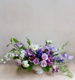 South Shore Garden - This arrangement with blooms in hues of lavender and plum is a lush treat for any occasion!  Arranged in a 6” wide white ceramic pot   Flowers pictured are representative of designer’s style, market availability and season. Due to this, the floral arrangement pictured will not always reflect the arrangement you will receive.