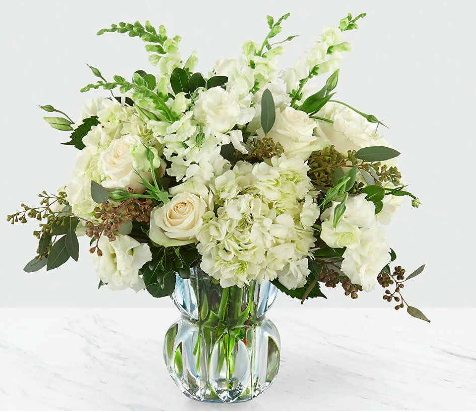Gala™ Luxury Bouquet - There's something about simplicity that just gives off the sense elegance. Comprised of classic white blooms and luscious greens set in a subtle blue heavyweight glass vase, the pure beauty of the bouquet instantly draws you in. Vendela roses, snapdragons, and hydrangea capture a truly refined bouquet. IMPRESSIVE bouquet is approx. 17''H x 17&quot;W. STUNNING bouquet is approx. 18&quot;H x 19&quot;W.
