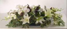 White Winter - Dinner centerpiece white lilies beautifully worked with white freesia, white twisted ribbon and pine.