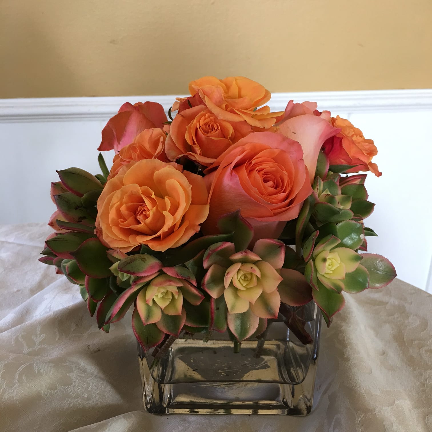 Delicious succulents - Bright orange roses with variegated orange succulents designed in clear glass container. 