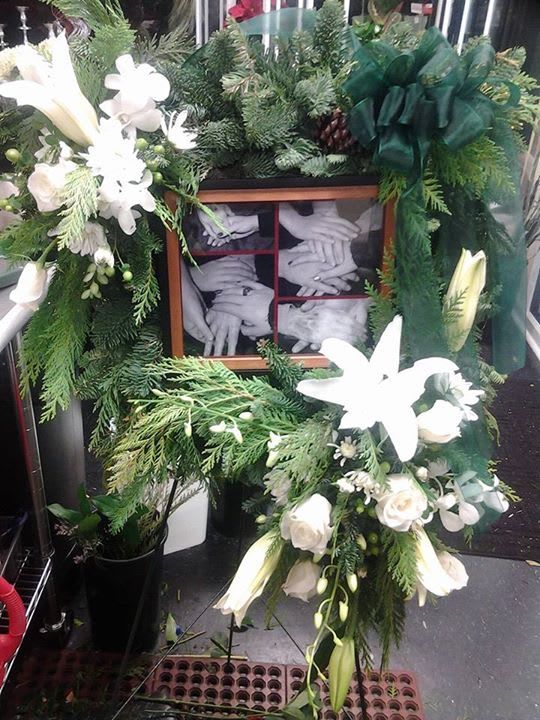 Your family tribute standing sqauare wreath - Square wreath in mixed winter greens with white lily blooms, green hypericum berries, roses, pomps and orchids. With your personal framed photo that will have that special meaning to you and your loved ones.