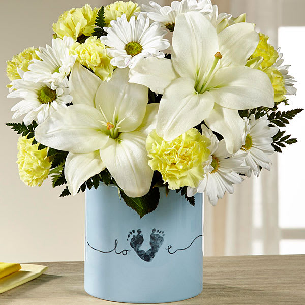 Tiny Miracle New Baby Boy Bouquet Tiny Miracle New Baby Boy Bouquet - The FTD® Tiny Miracle™ New Baby Boy Bouquet is the perfect way to send your happy wishes to the new family! Blooming with warmth and sunlight this gorgeous flower bouquet brings together yellow roses yellow carnations yellow mini carnations white Asiatic Lilies and white traditional daisies to create a memorable gift. Presented in a keepsake blue ceramic vase with "Love" written in a script font on the front and the print of a baby's foot making up the 'V' in the word for a sweet and touching affect this fresh flower arrangement is a wonderful way to send your congratulations to friends and family at this joyful time in their lives. GOOD bouquet includes 10 stems. Bouquet has pprox. 13"H x 11"W.
