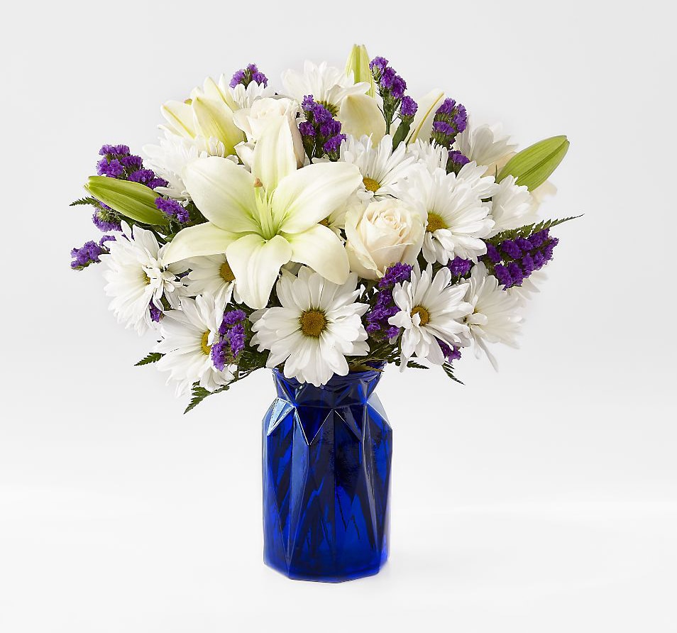 The Beyond Blue Bouquet The Beyond Blue Bouquet - The Beyond Blue Bouquet is a wonderful way to send peaceful wishes to your special recipient. Bringing together gorgeous white Asiatic Lilies, white roses, and white mini carnations accented with blue statice, and lush greens, this stunning bouquet captivates at every turn. Presented in a cobalt blue geometric glass vase to contrast with it's bright white blooms, this beautiful flower arrangement will make an excellent thank you, get well, engagement or sympathy gift. Bouquet includes 9 stems with vase. Approx. 14"H x 12"W.