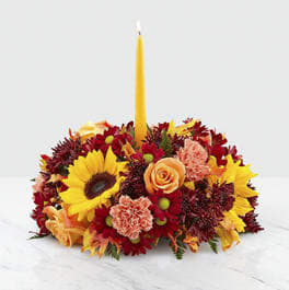 Giving Thanks Candle Centerpiece Giving Thanks Candle Centerpiece - Gather around a gorgeous centerpiece this harvest season. Our Giving Thanks Centerpiece is sure to add a touch of heartfelt warmth to any celebration with its collection of orange roses, sunflowers, glycerized oak leaves and orange carnations set around a golden taper candle. Whether you're a guest or the host, complete the table with an elegant centerpiece sure to brighten up the room.