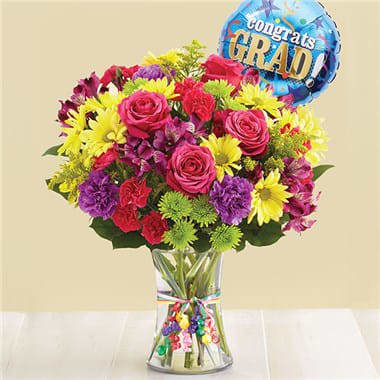 1-800-Flowers® It's Your Day Bouquet® For Graduation 1-800-Flowers® It's Your Day Bouquet® For Graduation - Every graduate deserves a day to celebrate, and we’ve got just the gift. Our hand-designed bouquet is brimming with the best and brightest blooms, gathered inside a charming vase, tied with ribbon. We’ve even included a festive balloon for an extra special way to remember their milestone! • All-around arrangement with hot pink roses and mini carnations, yellow daisy poms, Athos poms, purple Peruvian lilies (alstroemeria) and carnations; accented with assorted greenery • Large arrangement measures overall approximately 16""H x 12""W • Medium arrangement measures overall approximately 15""H x 11.5""W • Small arrangement measures overall approximately 14""H x 11""W • Artistically designed in a clear glass vase tied with colorful ribbon; vase measures 8""H • Includes an 18""D Mylar graduation balloon • Our florists hand-design each arrangement, so colors, varieties, container and balloon may vary due to local availability • To ensure lasting beauty, Peruvian lilies may arrive in bud form, and will fully bloom over the next few days"