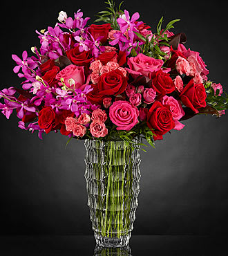 Heart's Wishes™ Luxury Bouquet - Deeply devoted to claiming your special recipient's heart with a bold mix of color saturated in it's finest form, this bouquet speaks to everlasting romance with each and every stem. Rich red roses mingle with the eye-catching hot pinks of Mokara Orchids, roses, and spray roses that help to convey your heart's every wish. Finished with lush green accents to delight the eye and make each bloom pop in it's intended way, this luxury bouquet arrives in a clear faceted glass vase lined with exotic red ti leaves to add even further interest to this already opulent design style. A gift of love that will surely touch their heart. IMPRESSIVE bouquet includes 41 stems. Approx. 24&quot;H x 26&quot;W. STUNNING bouquet includes 55 stems. Approx. 25&quot;H x 27&quot;W. Your purchase includes a complimentary personalized gift message.