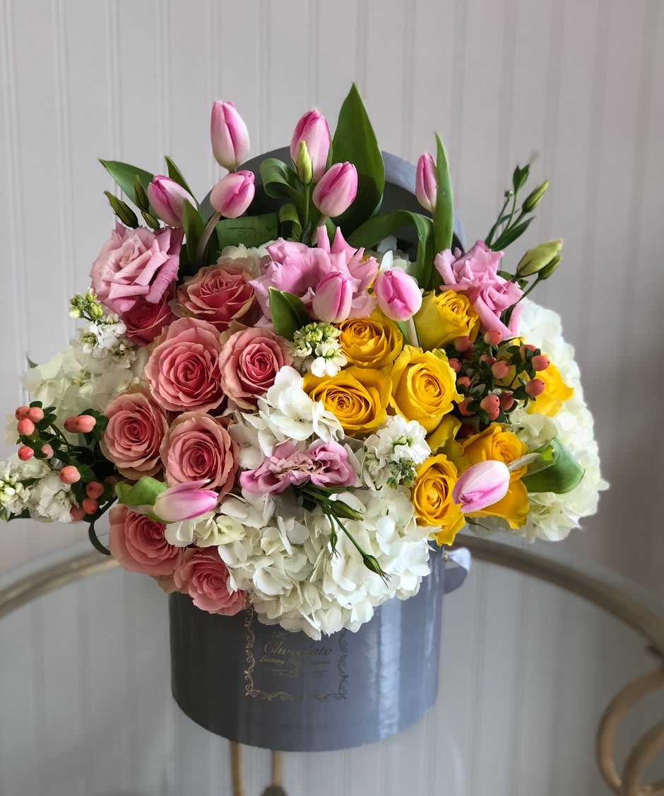 Bella - Hypericum Berries, Tulips, Licentious, Lush White Hydrangeas and more! - This Chocolato arrangement is made with yellow and pink roses, hypericum berries, pink tulips, licentious, and lush white hydrangeas. The arrangement comes in a grey round box.   Please see care instructions for further assistance on taking care of your Chocolato Boxed Flowers.  All prices are subject to change due to season and availability of fresh flowers. The arrangement seen is what will be made unless any substitution may need to be made based on season and availability of flowers.