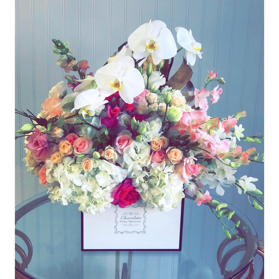 Charlotte - Phalaenopsis Orchids, Dendrobium Orchids, Roses, Spray Roses, Snapdragon and More! - This Chocolato arrangement is made with phalaenopsis orchids, dendrobium orchids, roses, spray roses, snap dragon, licentious, greenery and lush white hydrangeas. The arrangement comes in a white square box with black boarders.  Please see care instructions for further assistance on taking care of your Chocolato Boxed Flowers.  All prices are subject to change due to season and availability of fresh flowers. The arrangement seen is what will be made unless any substitution may need to be made based on season and availability of flowers.