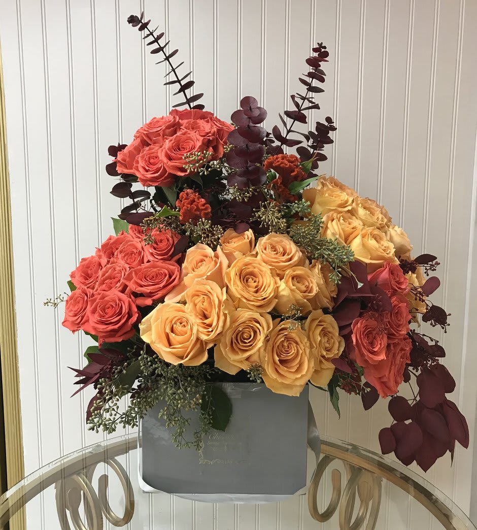 Isla - Roses, Eucalyptus, and Greenery - This Chocolato arrangement is made with light and dark orange roses, eucalyptus and greenery. The arrangement comes in a grey square box.   Please see care instructions for further assistance on taking care of your Chocolato Boxed Flowers.  All prices are subject to change due to season and availability of fresh flowers. The arrangement seen is what will be made unless any substitution may need to be made based on season and availability of flowers.