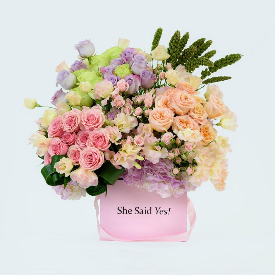 Mia - Roses, Spray Roses, Purple Hydrangeas and more! - This Chocolato arrangement is made with light orange, lavender and purple roses, spray roses, licentious, greenery and lush green and purple hydrangeas. The arrangement comes in a pink square box.   The message on the box is optional, if you do wish to have a special message please make sure to add the text in the notes box during checkout. Maximum size of message can be up to 20 characters.  Please see care instructions for further assistance on taking care of your Chocolato Boxed Flowers.  All prices are subject to change due to season and availability of fresh flowers. The arrangement seen is what will be made unless any substitution may need to be made based on season and availability of flowers.
