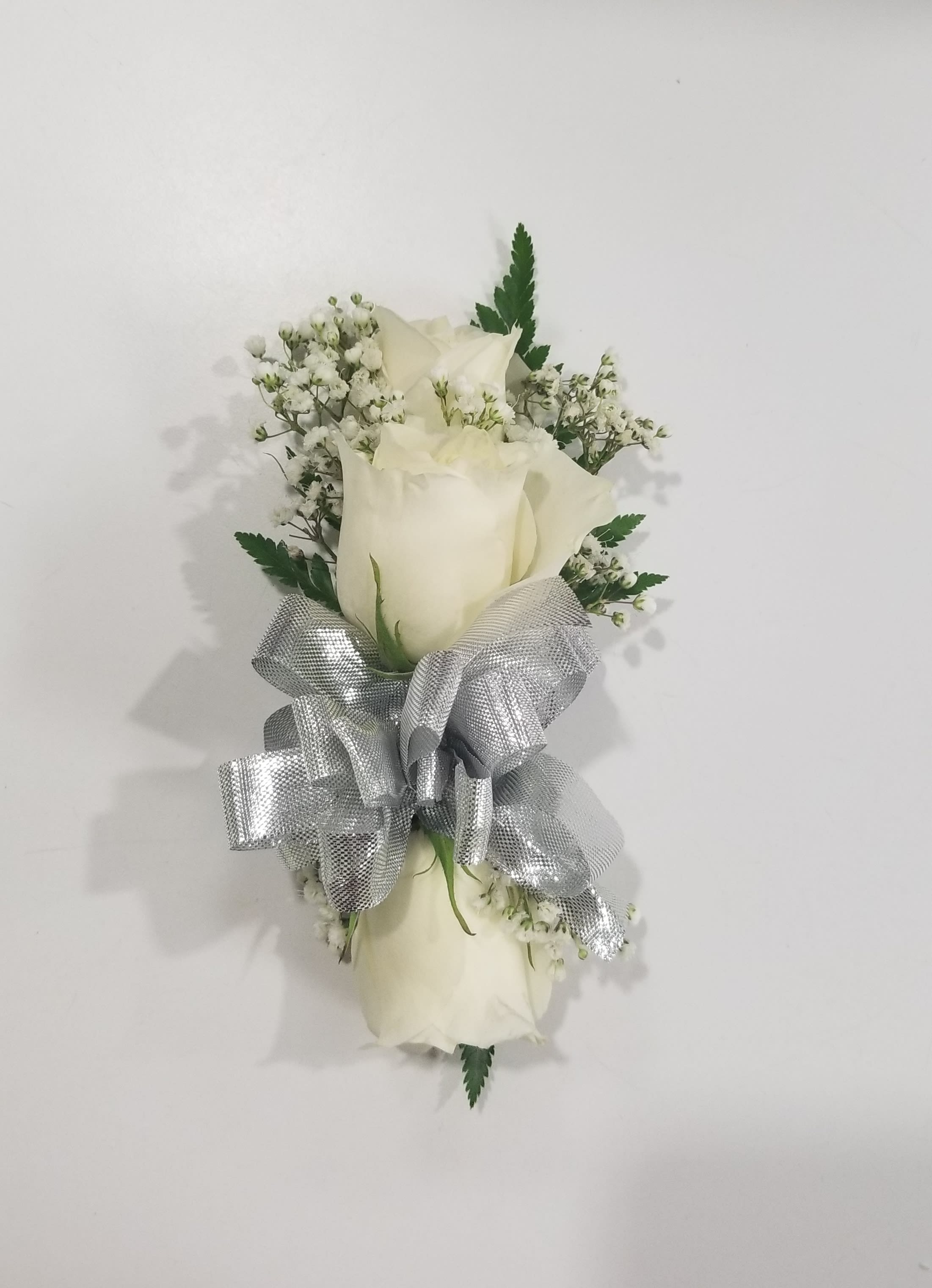 White Rose Wrist Corsage with Silver Bow - This is a beautiful, simple wrist corsage that comes dressed with greens, baby's breath and a silver bow. It is great for proms, wedding, and events. 