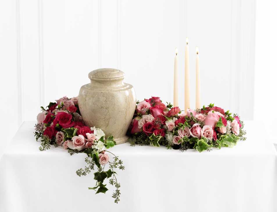 The FTD Remembrance Arrangement - The FTD Remembrance Arrangement is a sweetly sophisticated way to display their urn at their final farewell service. Fuchsia and pale pink roses and spray roses are accented with lush greens to form an exquisite arrangement that winds around the base of the urn and curls around 3 ivory taper candles, creating a warm and comforting presentation that commemorates a life that brought kindness and beauty in to the lives of others.