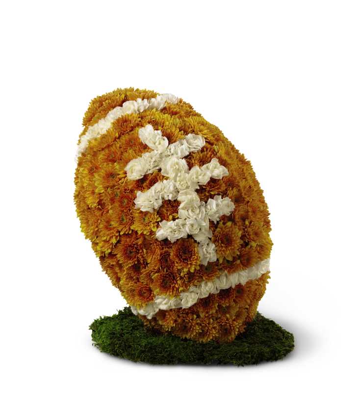 American Football Tribute - The American Football Tribute is a memorable and unique way to celebrate this beloved pastime so cherished by your loved one. Bronze chrysanthemums and white mini carnations form the shape and likeness of a football standing on a piece of lush green moss.
