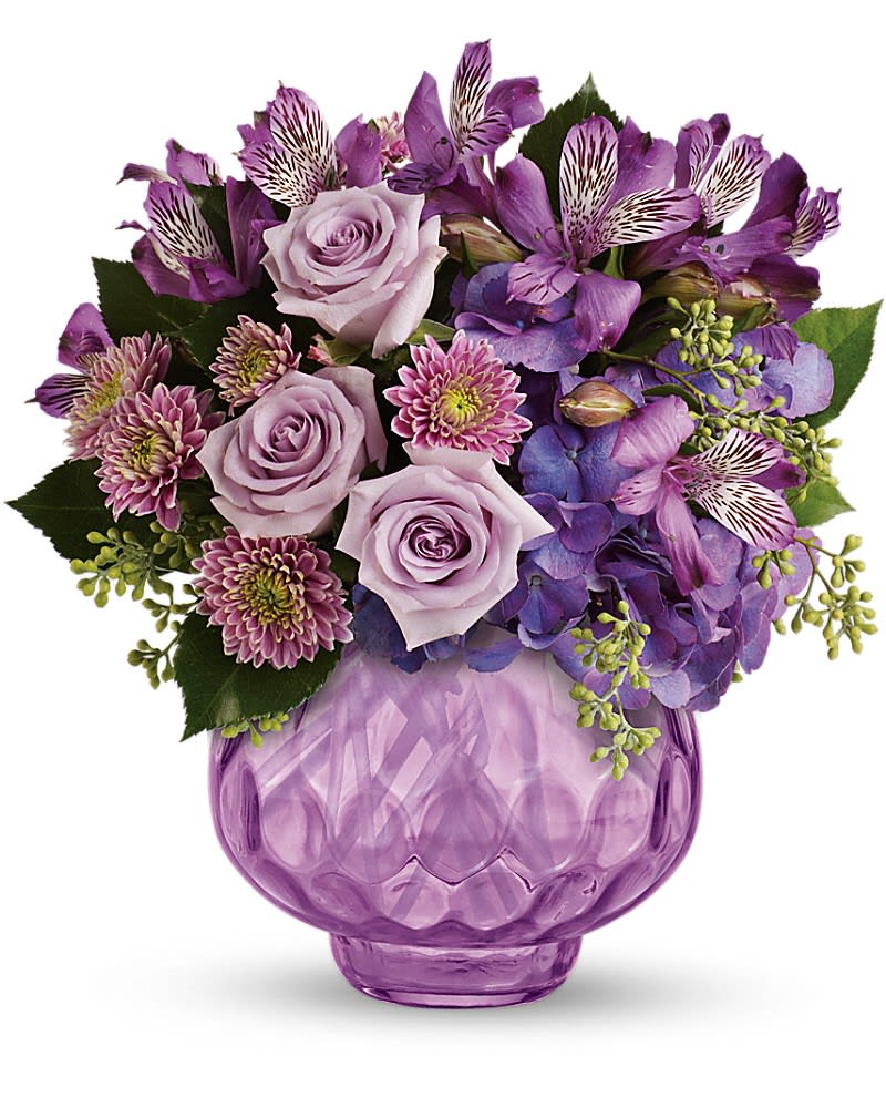 Teleflora's Lush and Lavender with Roses - Delightfully dramatic this gorgeous array of lavender and purple flowers in a lavender cut-glass votive bowl makes an enchanting gift. They&#039;ll love the flowers and bask in the glow of lavender candlelight for years to come. The ravishing bouquet includes purple hydrangea lavender roses purple alstroemeria and lavender cushion spray chrysanthemums accented with fresh greenery. Delivered in a stunning lavender cut-glass votive bowl.