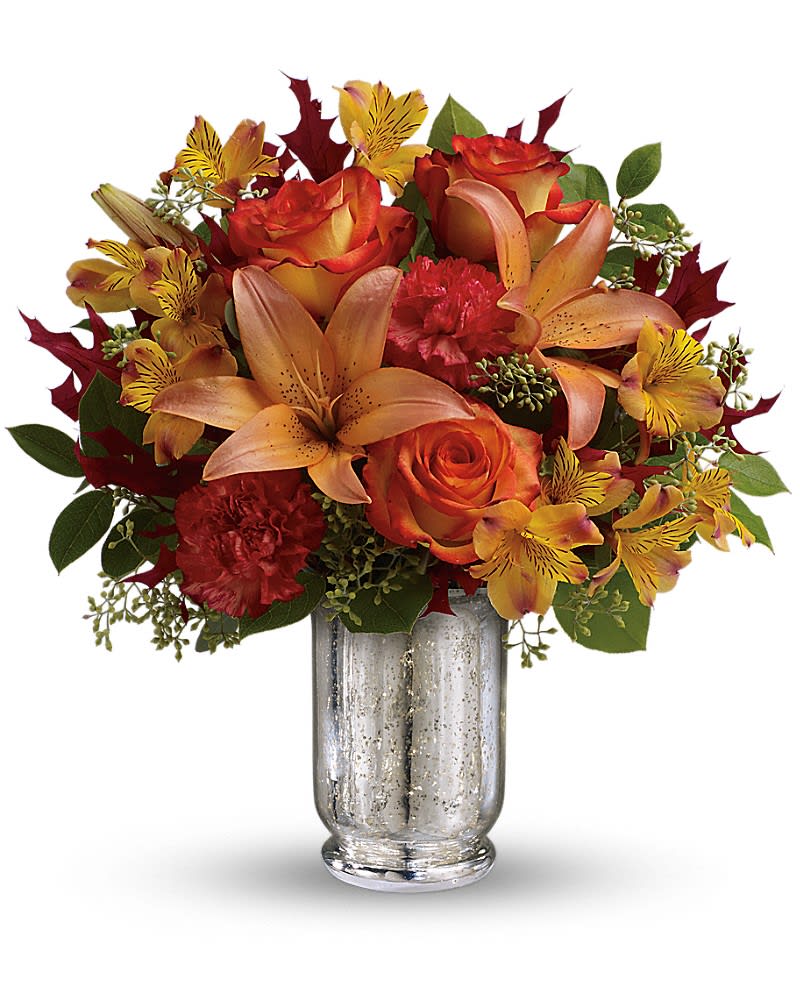 Teleflora's Fall Blush Bouquet - This fall make that special someone blush with joy! Gorgeous bi-color roses and lilies brighten their day while the magnificent mercury glass hurricane vase is a sparkling gift they&#039;ll always cherish. Stunning orange bi-color roses are arranged with orange asiatic lilies yellow alstroemeria dark orange carnations seeded eucalyptus lemon leaf and oak leaves. Delivered in an exclusive silver Mercury Glass hurricane.