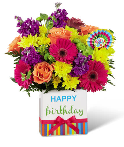 Birthday Brights™ Bouquet Birthday Brights™ Bouquet - Delight your special recipient on their big day with hot pink gerbera daisies, purple stock, yellow chrysanthemums, green button poms, bupleurum, and lush greens in a modern rectangular ceramic vase with colorful striping at the bottom, "Happy Birthday" lettering at the top, and a bright pink bow at the center.
