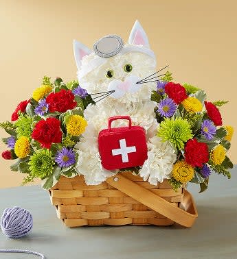  Cure-All Kitty™ - EXCLUSIVE Looking for the purr-fect remedy to help them feel better? Our feline M.D. loves to make house calls! This cute, cure-all creation is surrounded by a bright bunch of blooms, and comes with her own doctor’s kit. Add an uplifting balloon to get them on the mend in no time! •One-sided 3D arrangement with white carnations; red mini carnations; Athos poms; yellow button poms; purple monte casino; accented with assorted greenery •Crafted in the shape of a cat, complete with eyes, ears, mouth, whiskers, doctor’s kit and head piece •Artistically designed in a handled, splitwood basket with liner; measures 7&quot;H 
