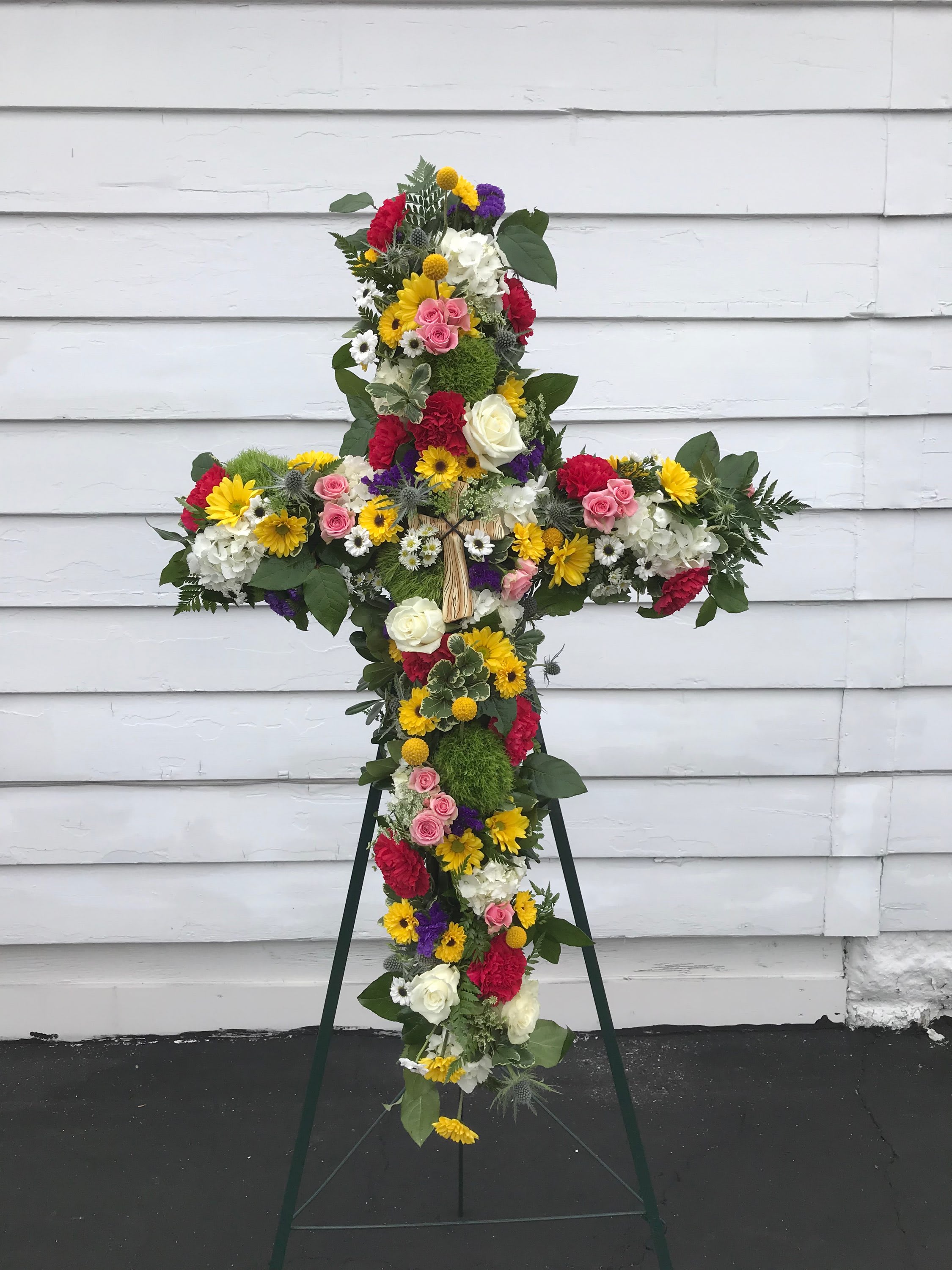 Cross Shaped Easel Spray Cross Shaped Easel Spray - A grand cross-shaped spray for the memorial of a loved one. Roses, daisies, spray roses, hydrangea, status and carnations make this a colorful expression of sympathy and memory. This spray is also accented with a resin cross in the center.