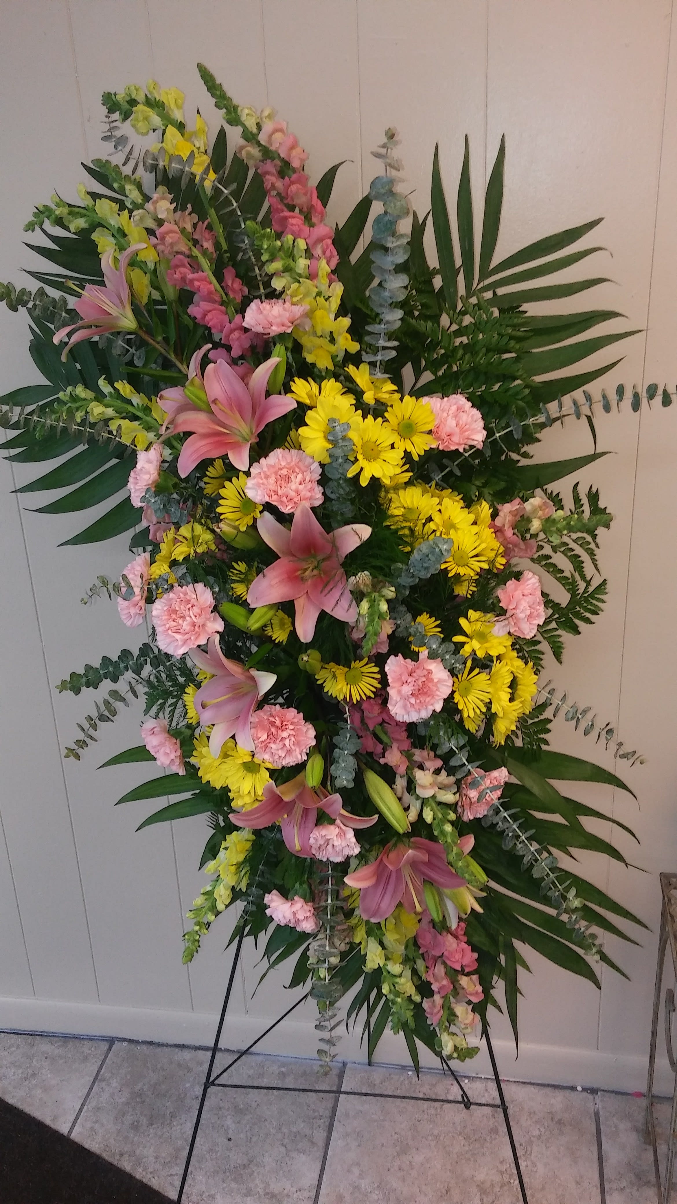 Honoring Someone Truly Special - This GRAND design will make a statement of enduring love and tribute, presented on an easel for ease of placement with elegant flowers including lilies, carnations, daisies, snapdragons, and fragrant eucalyptus. It is fit to honor someone truly special. We can even ADD or SUBSTITUTE their favorite flowers or colors (with some notice, and a phone call to us). ***This Standing Spray can also be made in ALL WHITE*** (Use special instructions for all white.) 