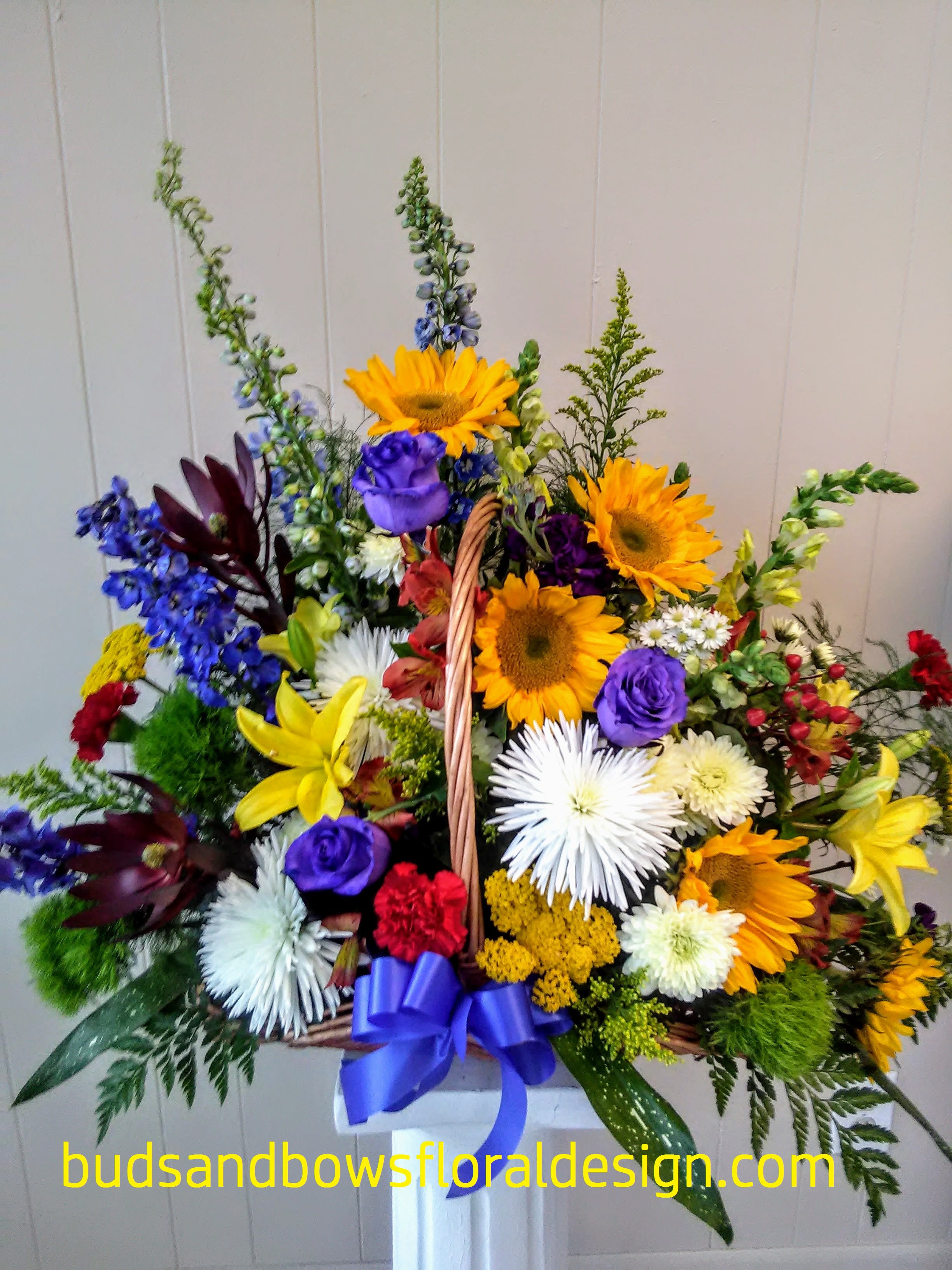 Fireside of Wildflowers Fireside of Wildflowers - There is not a more heartfelt way to express your sorrow than with this fireside basket filled with flowers. This basket was inspired by wildflowers in a field, featuring flowers such as sunflowers, chrysanthemums, leucadendron, carnations, and Peruvian lilies, as well as a bunch of different colors and textures. It also has 3 roses which have been sprayed/dyed blue for effect! This is the perfect choice to convey warm and special feelings of sympathy and remembrance.