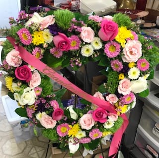 Open Heart Wreath - A mixed assortment of flowers and colors to include roses, cushion mums, and daisies in pinks, yellows, and whites nestled in greenery. 