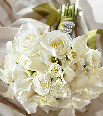 Serene Highness™ Bouquet - Clean and bright, white roses and spray roses are arranged to perfection with mini calla lilies as the stems are wrapped in sparkling green taffeta ribbon and accented with oval crystal brooches for a glittering affect. 