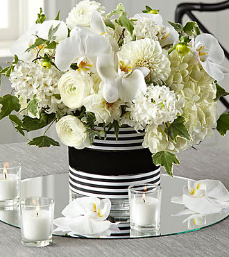 Solemnity™ Arrangement - White ranunculus, dahlia, hyacinth, hydrangea, and phalaenopsis orchids are arranged with an artist's eye, accented with variegated ivy vines. Presented in a clear glass cylindrical vase wrapped in black and white striped ribbon at the top and bottom and black soft velvet ribbon at the center, this gorgeous bouquet is a wonderful way to celebrate your love in a fresh modern way.
